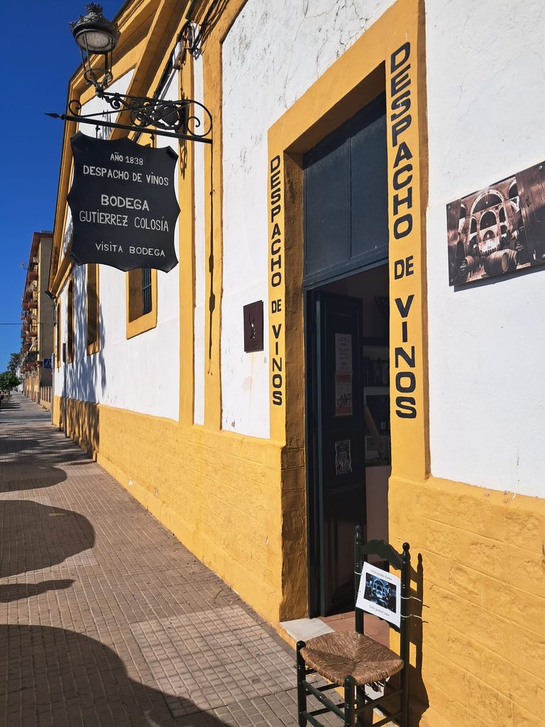 Close-up of entrance with "Año 1838 / Despacho de Vinos / Bodega Gutiérrez Colosía" sign, and yellow-framed Despacho de Vinos doorway